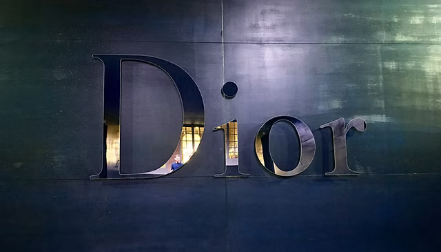 Large Dior signage on a dark metallic wall, a figure reflected in the polished surface