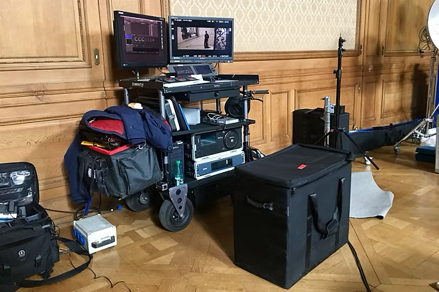 A D.I.T cart with two monitors, bags and flight cases set up in a wood-panelled room